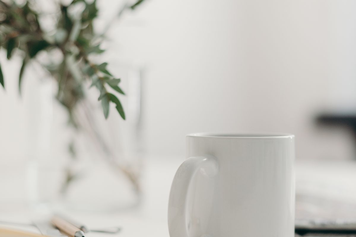 A white mug and an open notebook on a bright desk