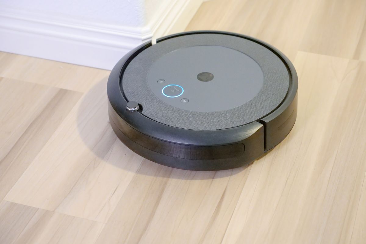 A dark robot vacuum cleaning along a skirting board on a wooden floor