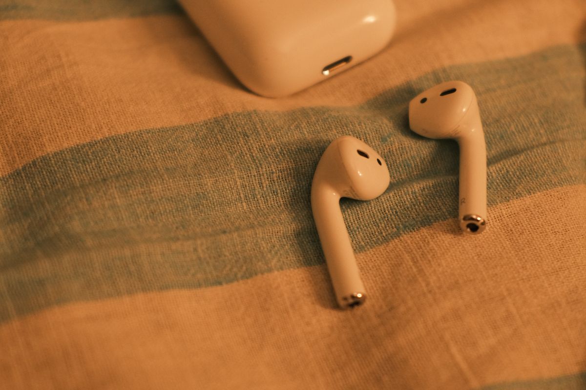Stem-style white earbuds and a charging case on striped fabric
